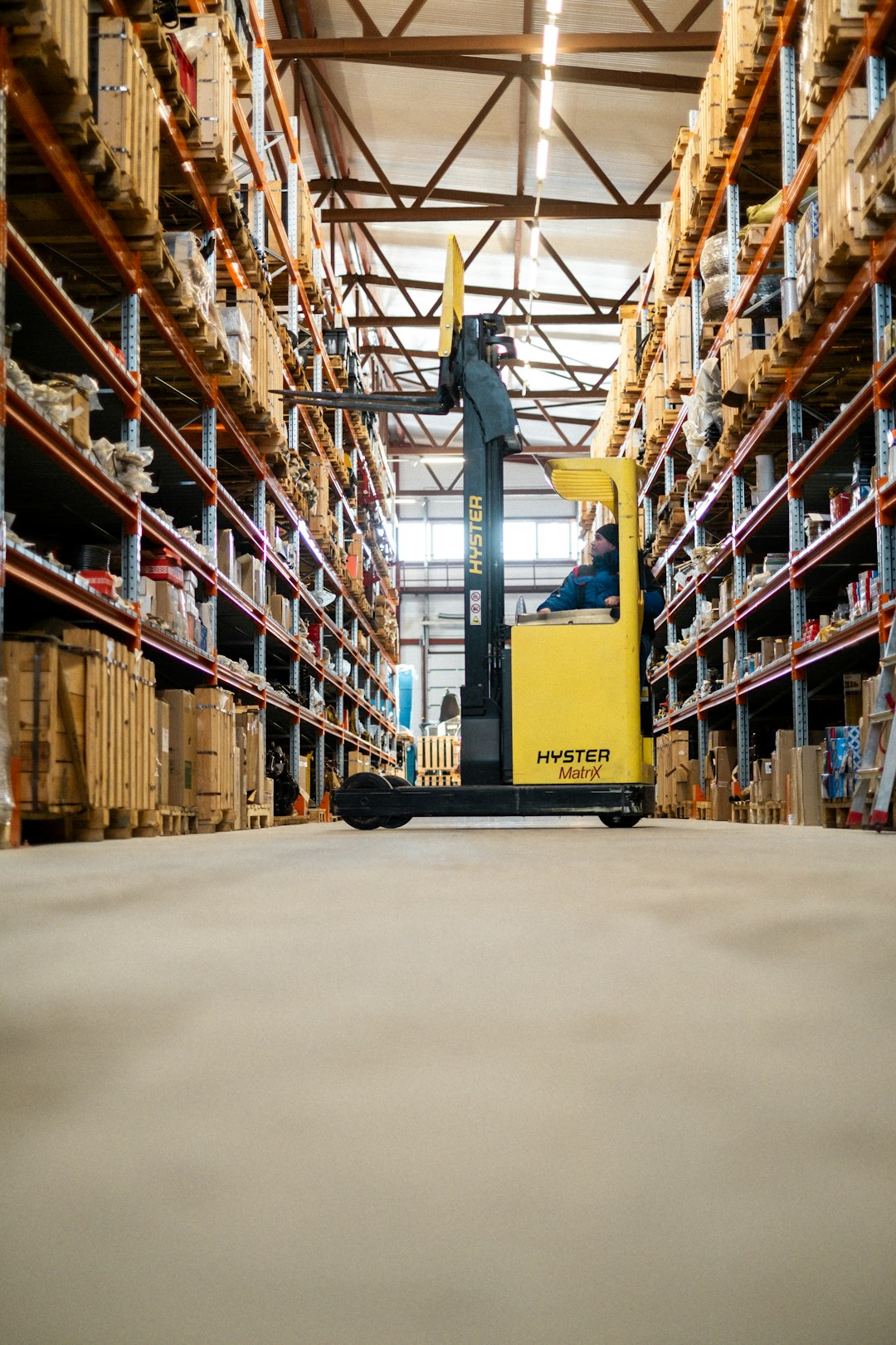 Crafting Captivating Headlines: Your awesome post title goes here Warehouse Worker Organizing Inventory on a Ladder A warehouse worker in blue overalls and a beanie is standing on a metal ladder, reaching for a package on a high shelf. The warehouse is filled with industrial shelves stocked with boxes and various supplies. The image captures the essence of logistics, inventory management, and manual labor in a structured warehouse environment.
